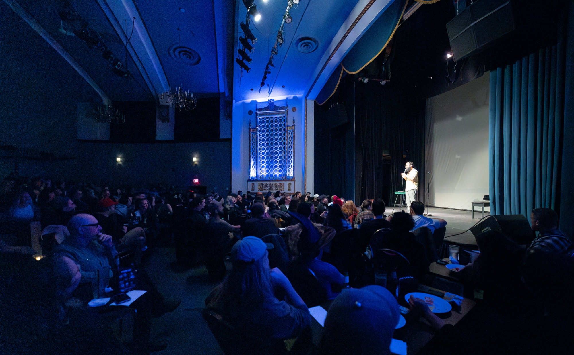 A full House of Comedy Vancouver room watching a performer on the lit stage beneath the venue's blue honeycomb wall